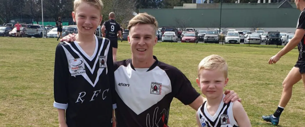A senior Ringwood Football Club player posing on the oval with two young Redbacks juniors in club jumpers